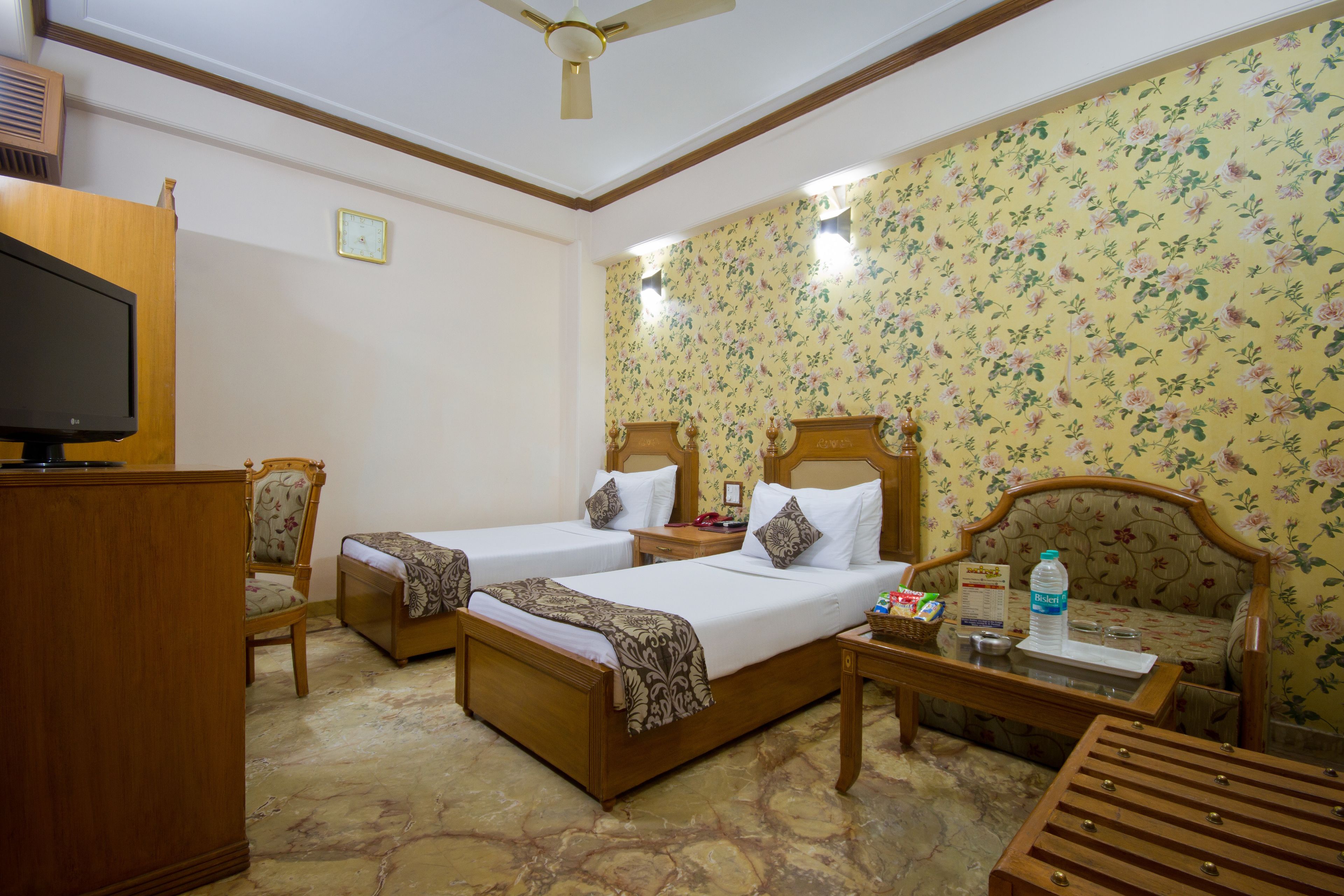 A hotel room with two beds, a wooden desk, a television, and a ceiling fan.