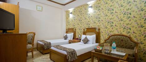 A hotel room with two beds, a wooden desk, a television, and a ceiling fan.