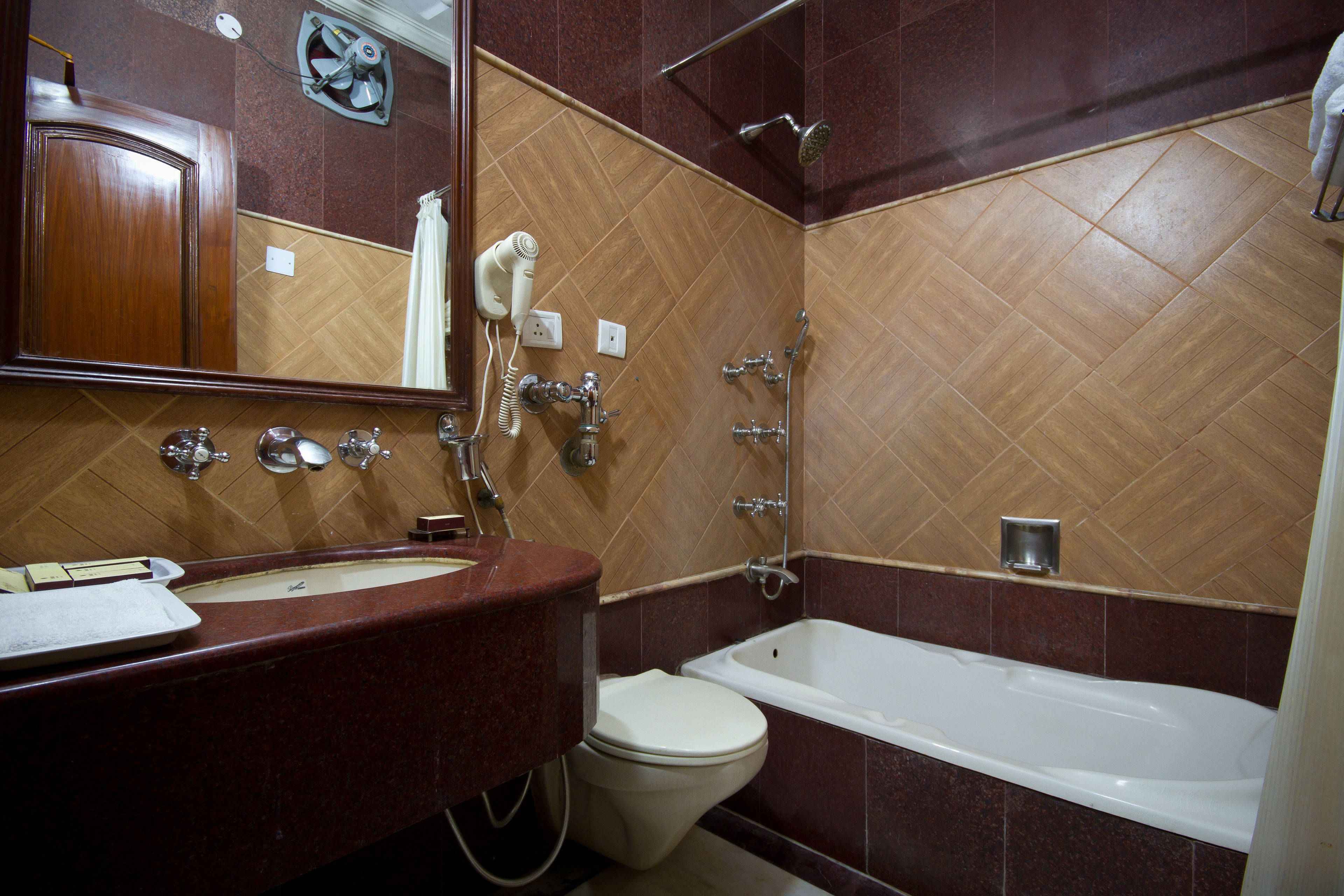 A bathroom with a wooden herringbone floor, a white bathtub, a toilet, and a vanity with a mirror.