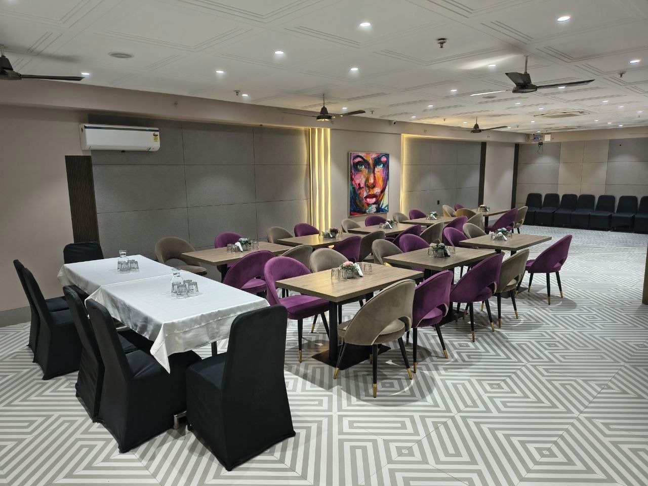A conference room with multiple tables and chairs, air conditioning units, and a ceiling fan.