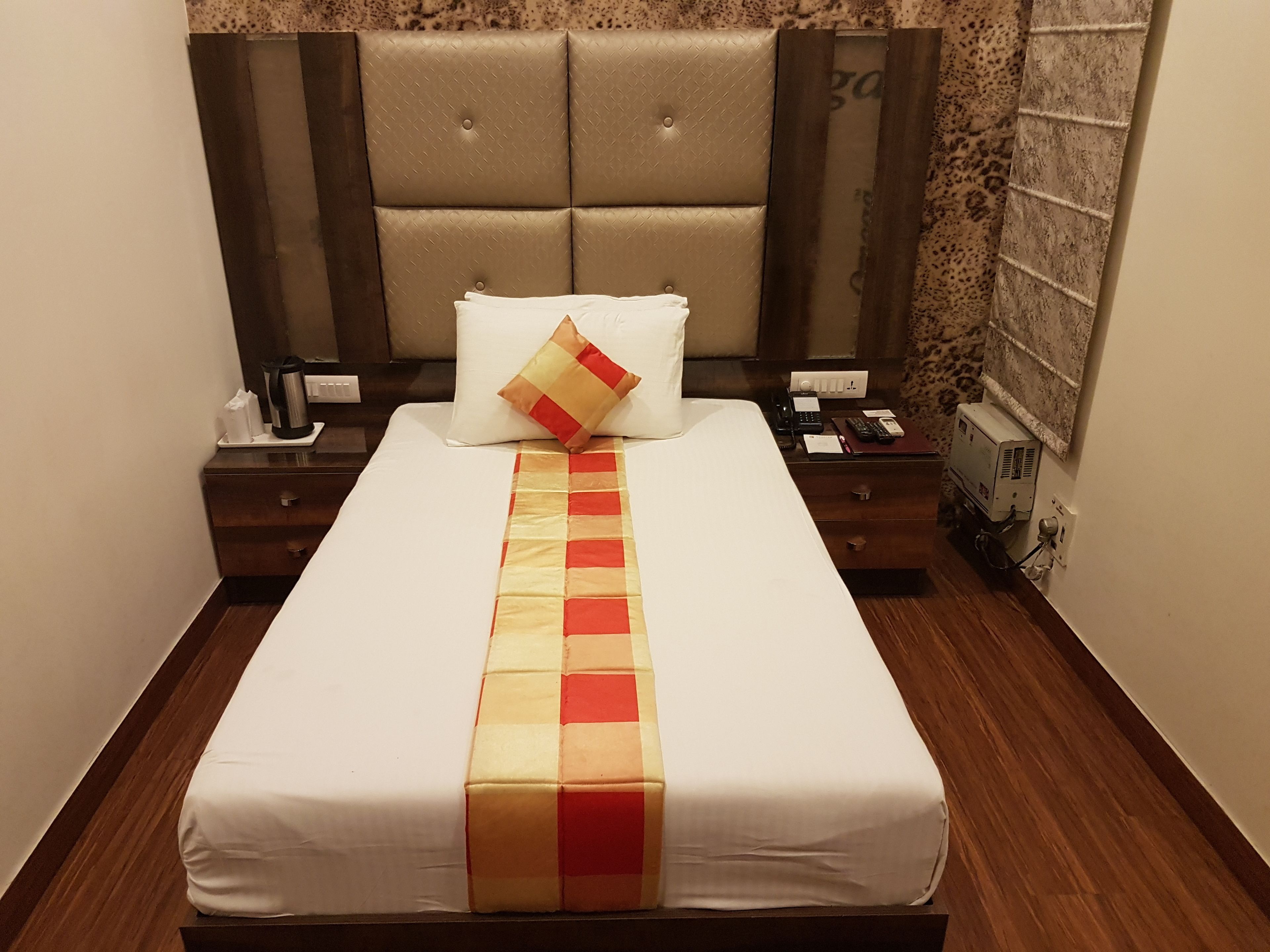 A neatly made bed with a white and red striped bedspread, a headboard with a diamond pattern, and a wooden nightstand with a phone and a small lamp.