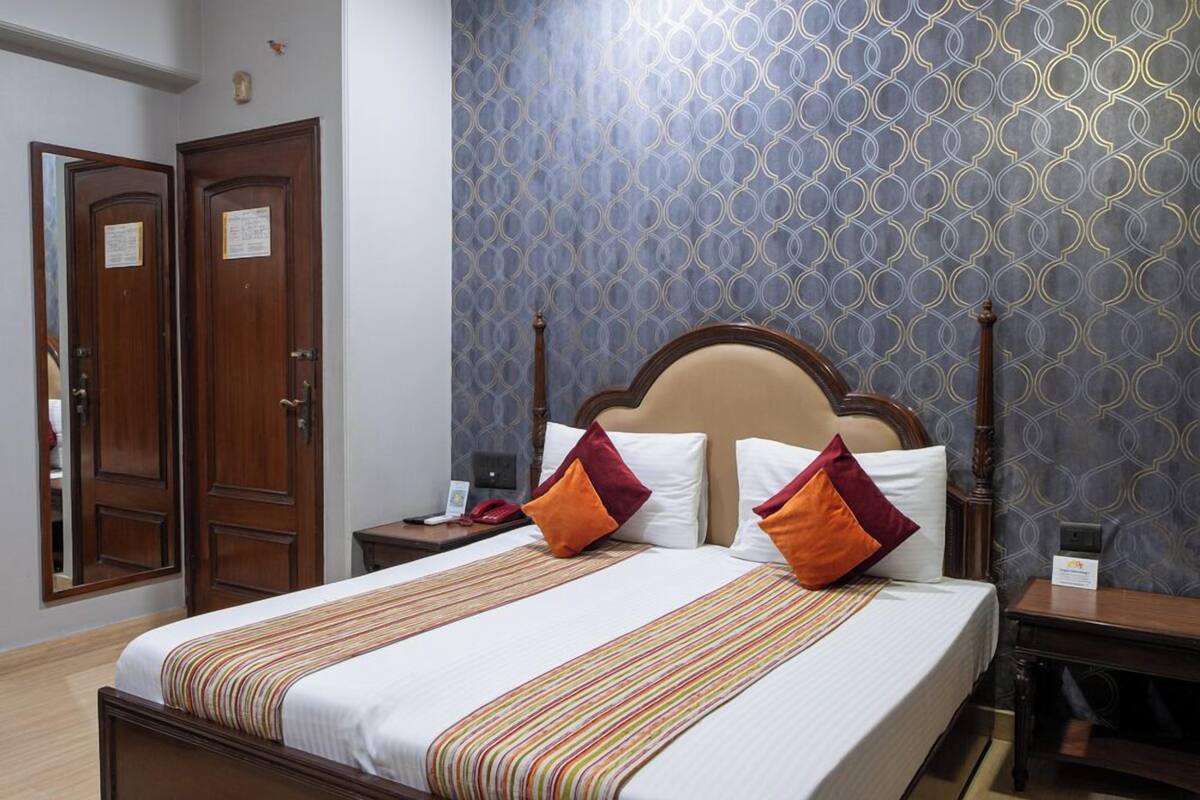 Habitación de hotel con cama, cabecero de madera y papel tapiz estampado.