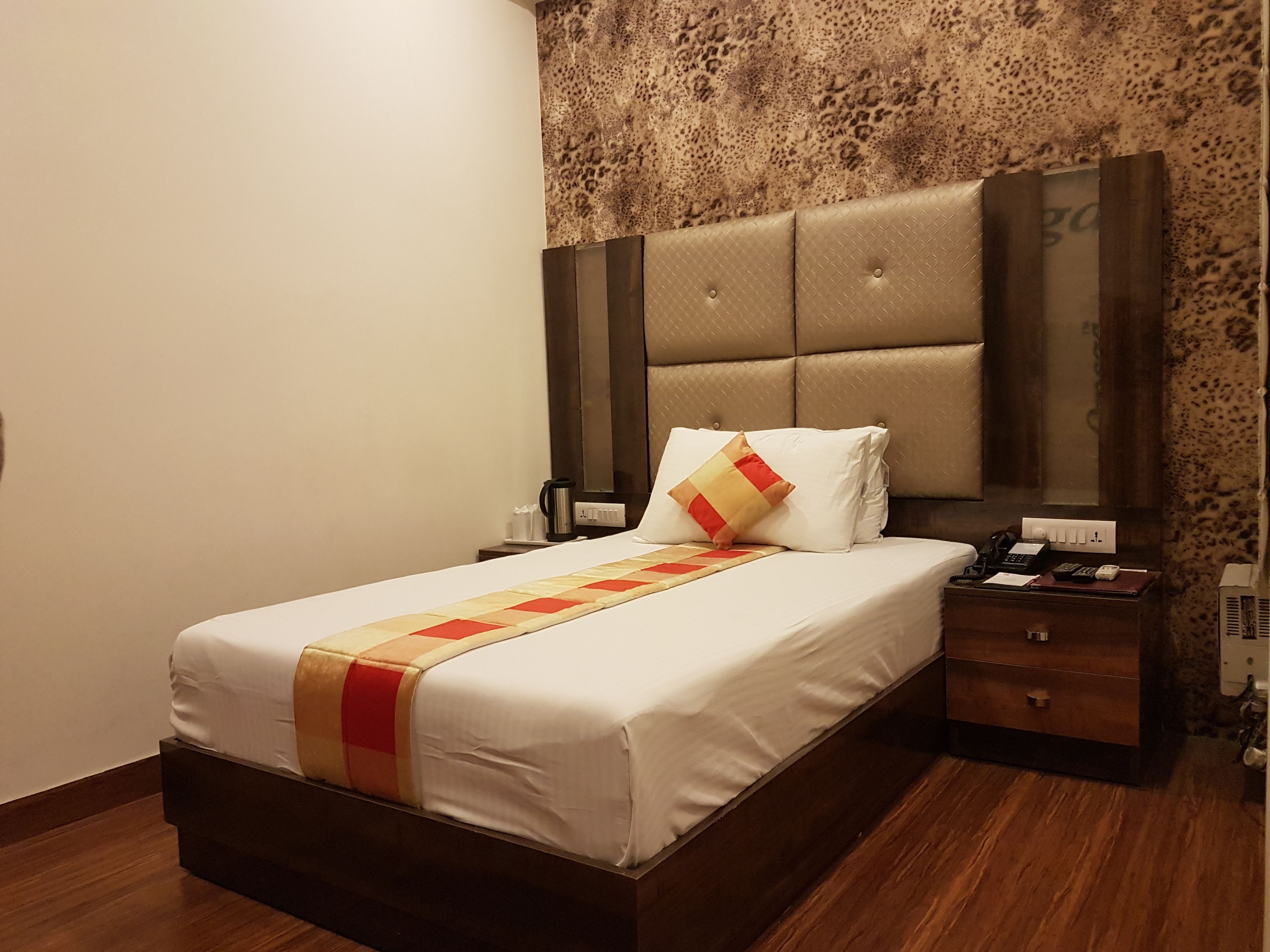 Una cama bien hecha con colcha, una mesita de noche con un teléfono y una lámpara, y una pared con un diseño texturizado.