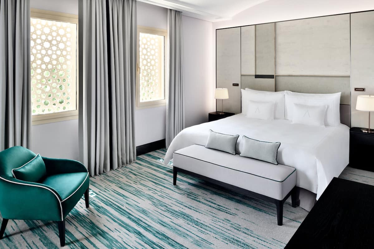 A hotel room with a bed, a chair, a nightstand, and a large window with curtains.