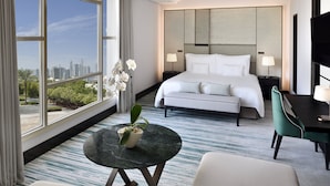 A hotel room with a large window, a bed, a desk, and a chair. - Address Montgomerie (Dubai)