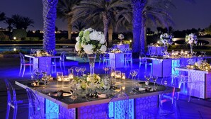 A formal outdoor dining area with clear tables, chairs, and floral centerpieces. - Address Montgomerie (Dubai)