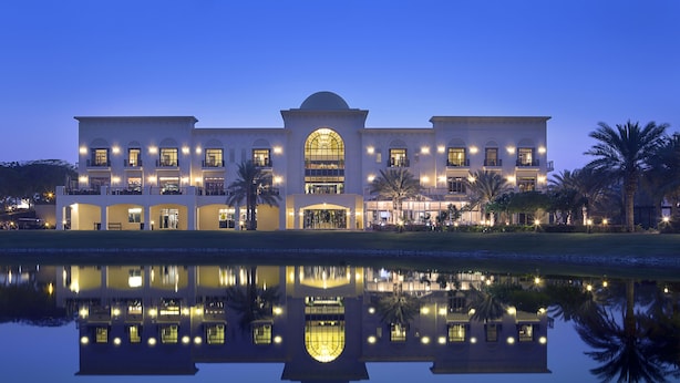 A large, multi-story hotel with a symmetrical facade, a central arched entrance, and a reflection in the water in front. - Address Montgomerie (Dubai)