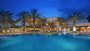 A hotel with a swimming pool, palm trees, and lounge chairs. - Address Montgomerie (Dubai)
