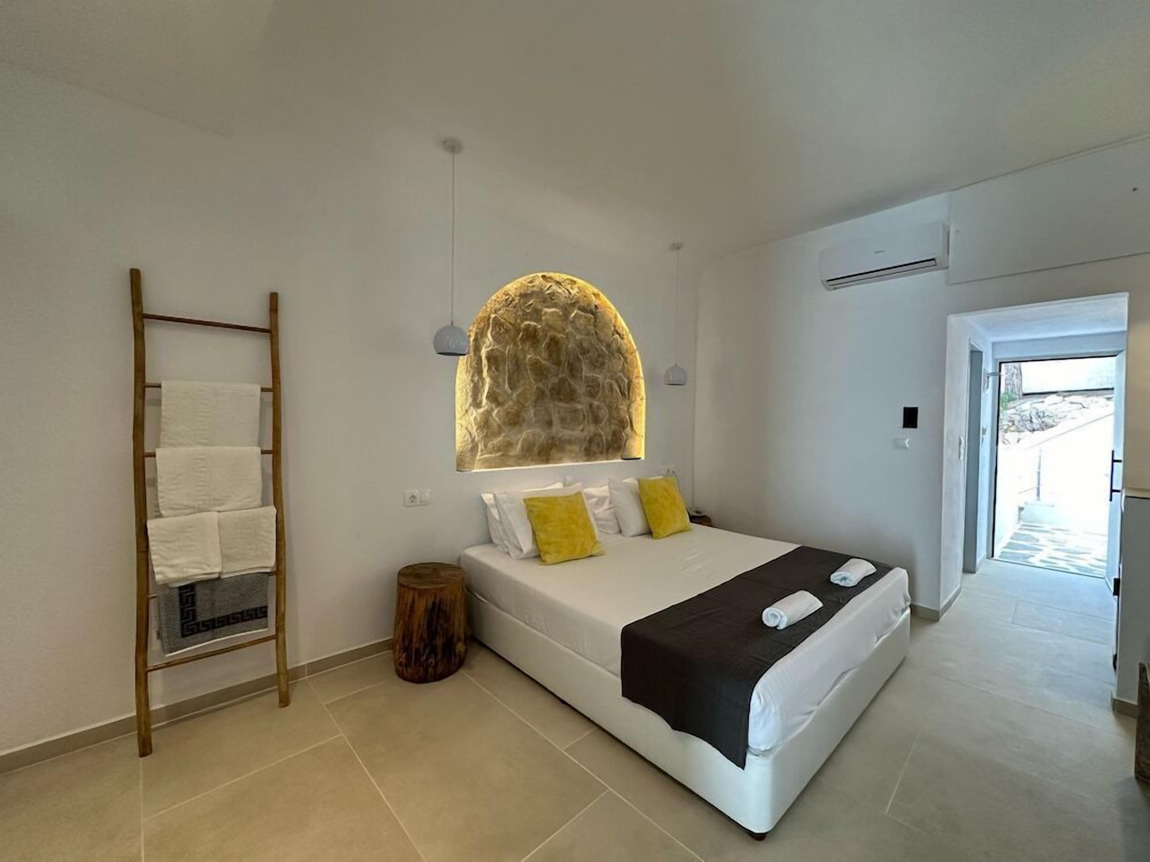 A bedroom with a bed, a wooden ladder, a stone wall, and a door leading outside.