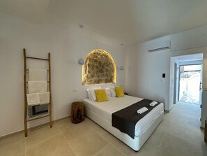 A bedroom with a bed, a wooden ladder, a stone wall, and a door leading outside. - Ladiko Hotel And Bungalows (Rhodes)