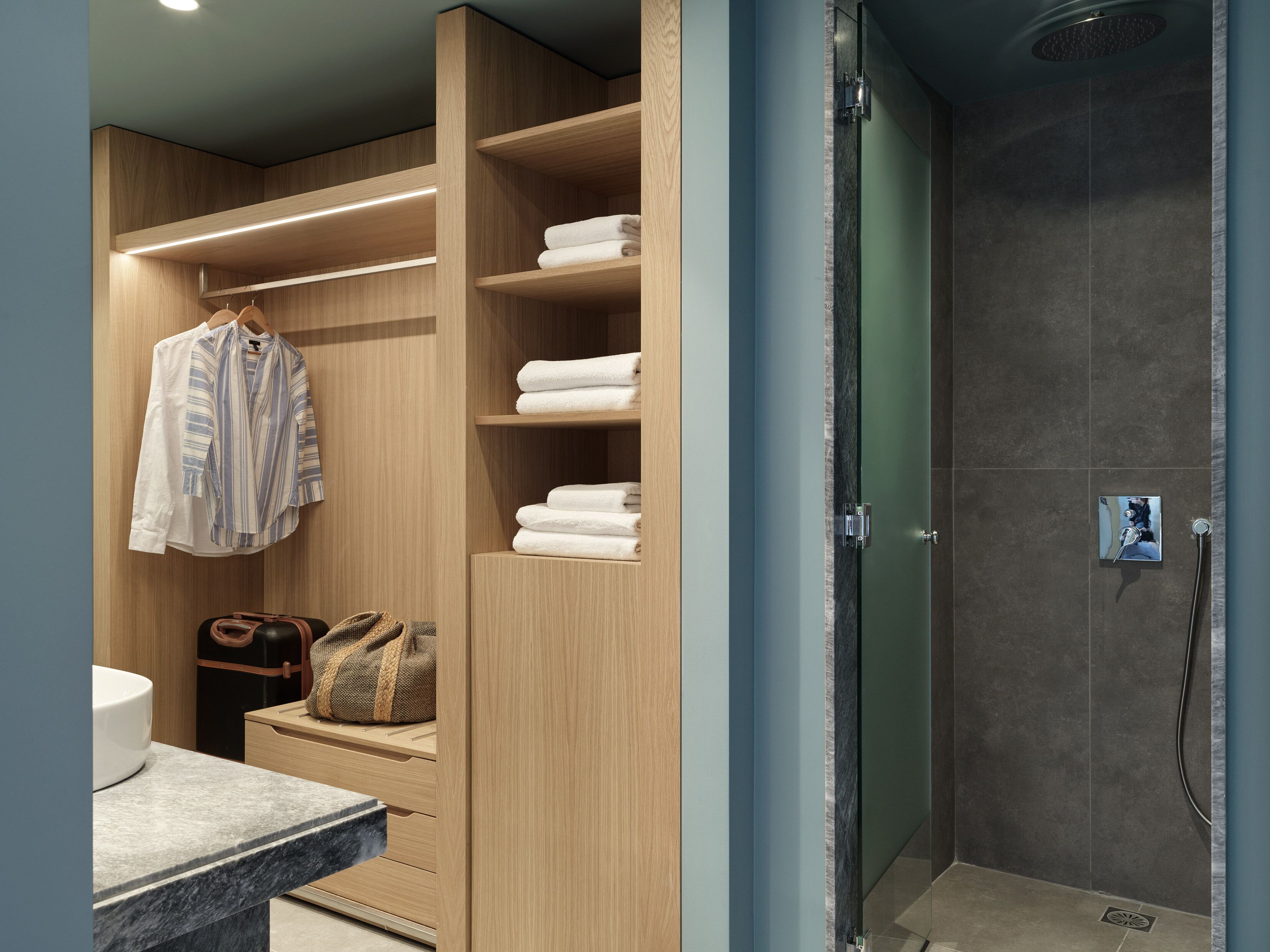 A modern bathroom with a walk-in shower, wooden storage, and a marble countertop.