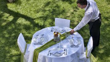A round table set outdoors with white tablecloths, green napkins, and white chairs.