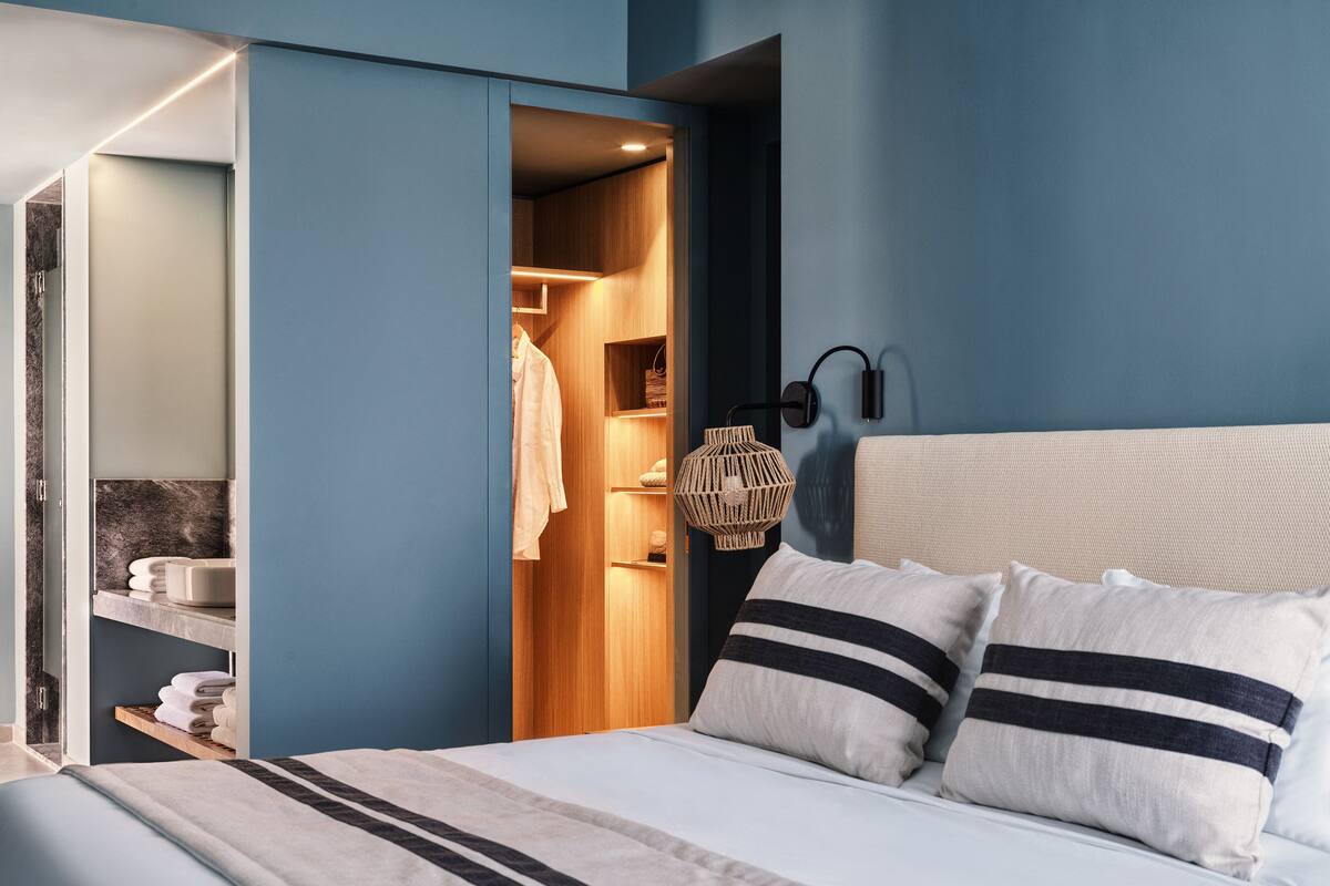 A modern bedroom with a bed, a nightstand, a built-in wardrobe, and a bathroom visible through an open door.