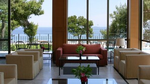 Un vaste espace intérieur doté de grandes fenêtres offrant une vue sur la mer. On y trouve plusieurs coins salon avec des canapés et des fauteuils.