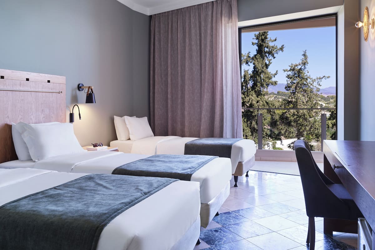 A hotel room with two beds, a desk, and a view of trees and mountains.