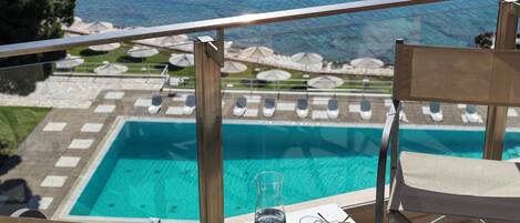 Un balcón con vista a una piscina, sillones de descanso y sombrillas.