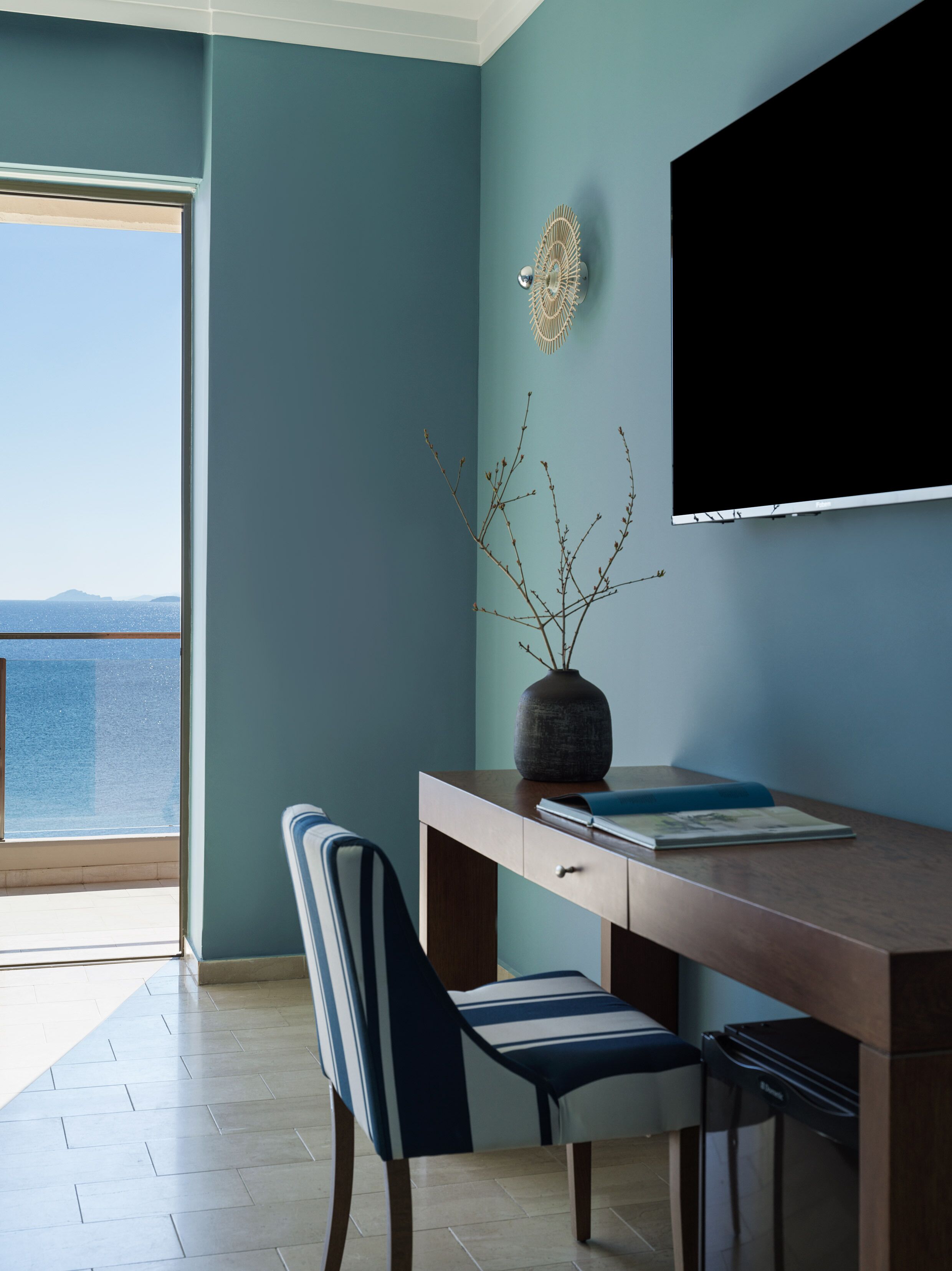 Une chambre moderne avec vue sur la mer, un bureau agrémenté d’un vase et une chaise.
