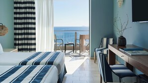 Une chambre d’hôtel avec deux lits, un bureau avec une chaise, une petite table, une télévision et une vue sur la mer.