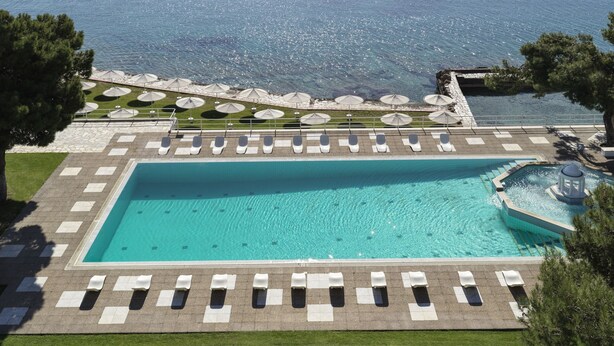 Un espace piscine doté de chaises longues et de parasols, offrant une vue sur une vaste étendue d’eau et sur des collines lointaines.