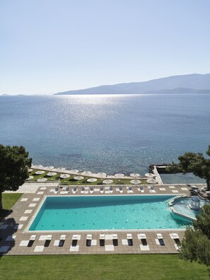 A pool area with lounge chairs and umbrellas, overlooking a large body of water and distant hills. - Kalamaki Beach Resort (Corinth)