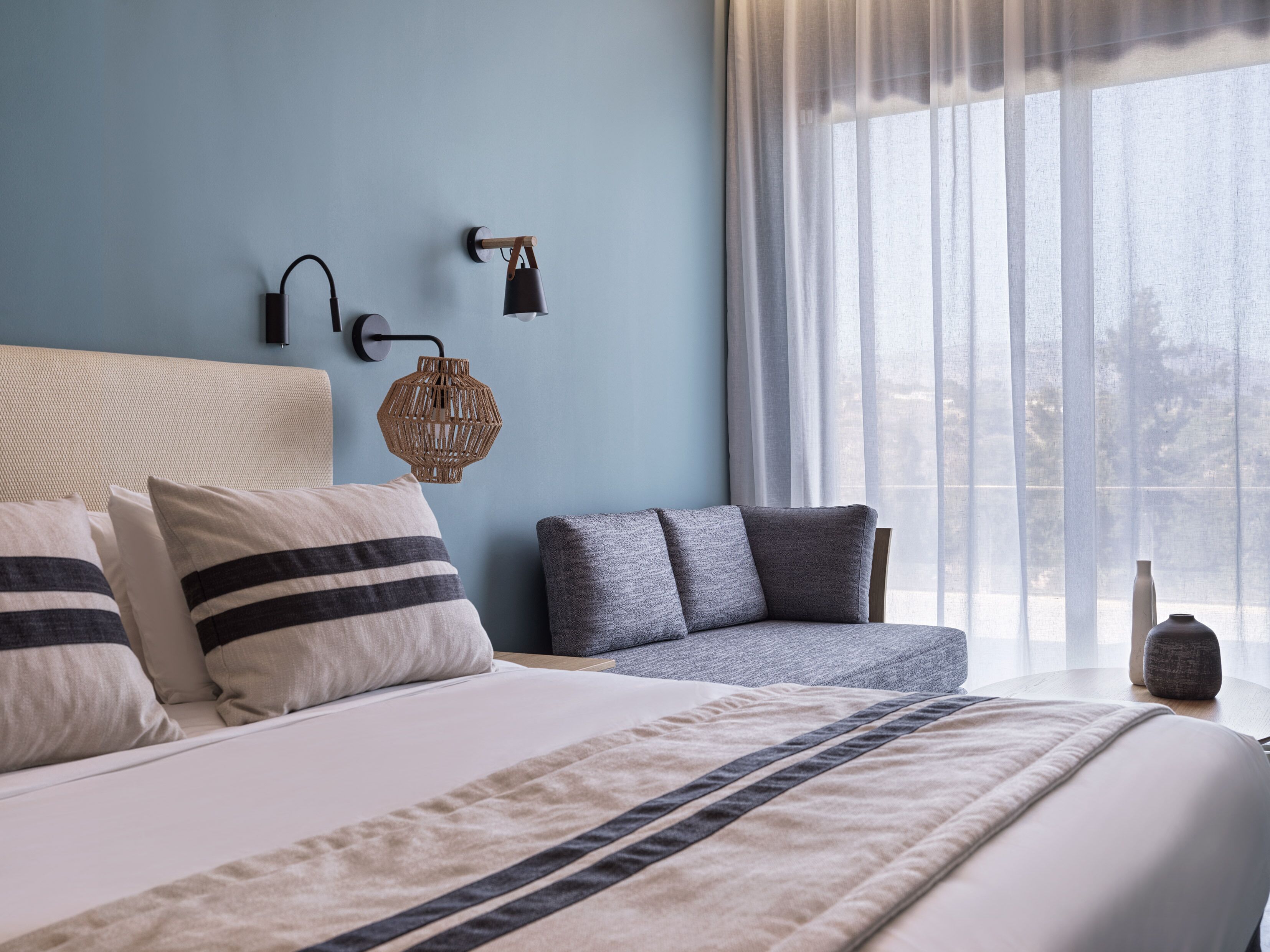 Una camera da letto con un letto, un divano, una lampada a parete e una finestra con tende leggere.