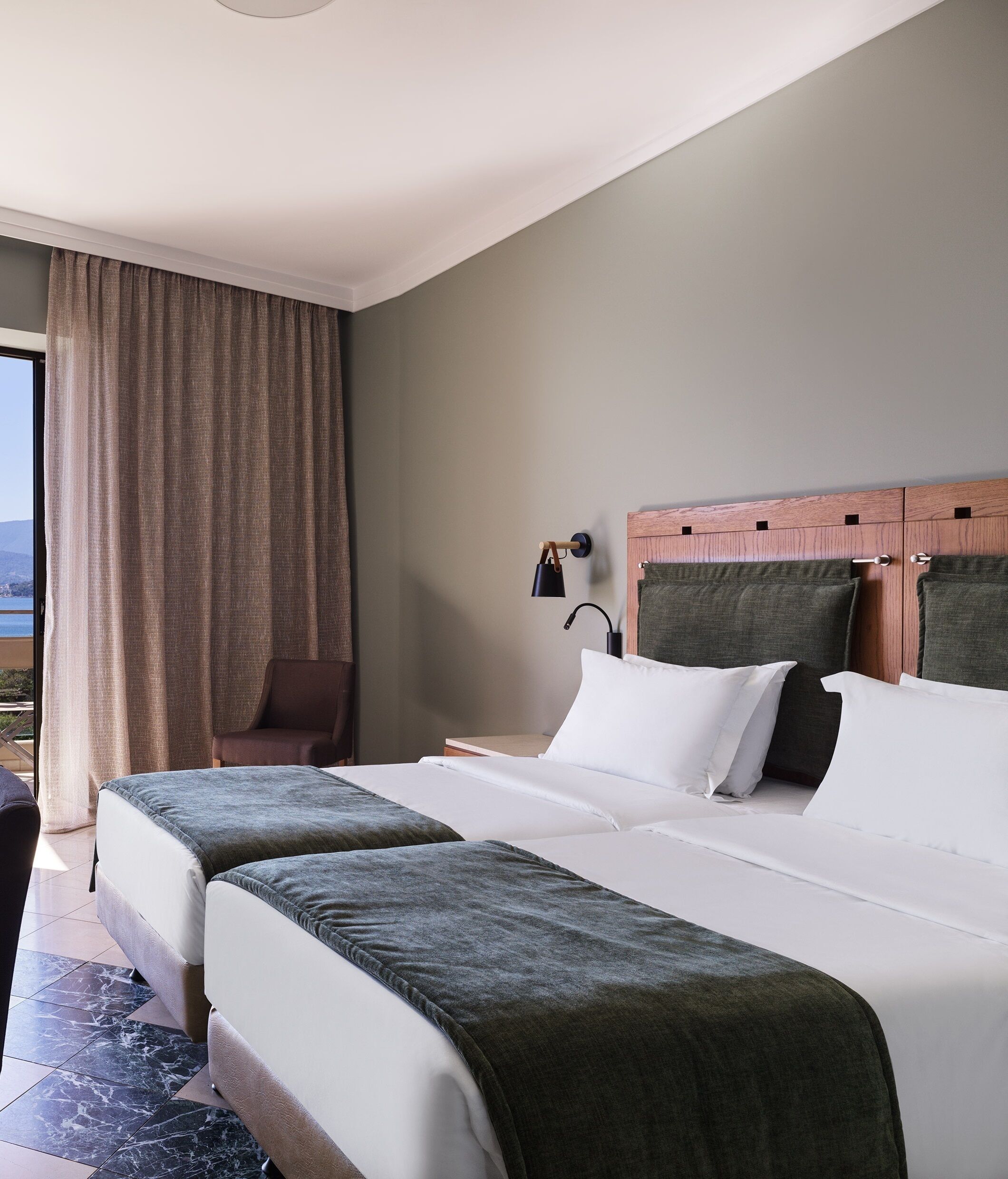 Ein Hotelzimmer mit zwei Betten, einem Schreibtisch, einem Stuhl, einer Lampe und Blick ins Freie.