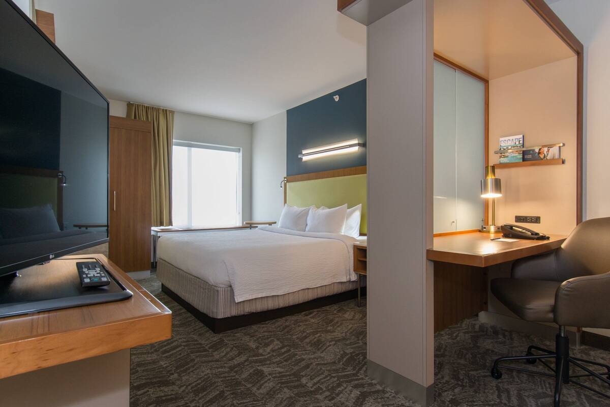 Een hotelkamer met een bed, een bureau met stoel, een televisie en een lamp.