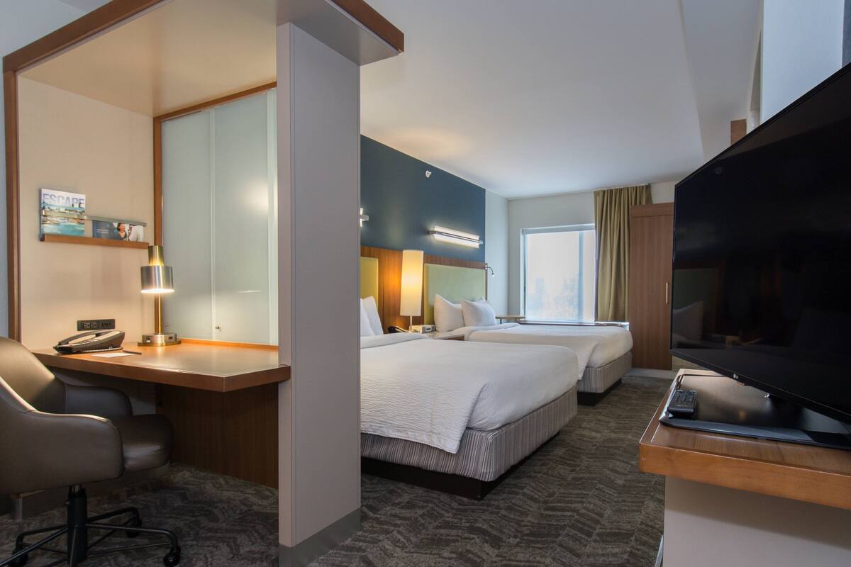Een hotelkamer met een bureau, twee bedden, een televisie en een grote spiegel.