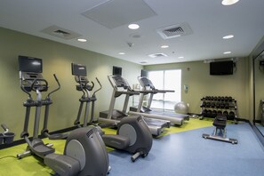 Een sportschool met loopbanden, elliptische trainers, een roeimachine en een bankdrukapparaat.