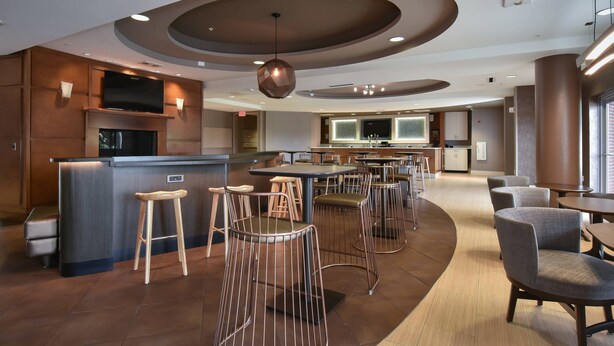 A modern restaurant with a bar area, wooden stools, and a curved seating arrangement. - SpringHill Suites by Marriott Columbia Downtown/The Vista (Columbia)