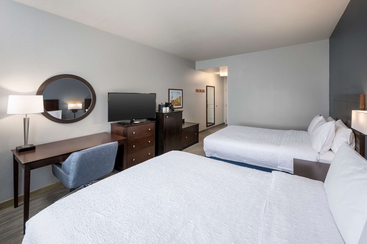 A hotel room with two beds, a desk with a chair, a TV, and a dresser.
