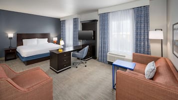 Una habitación de hotel con cama, escritorio, dos sillones, televisión y ventana con cortinas.