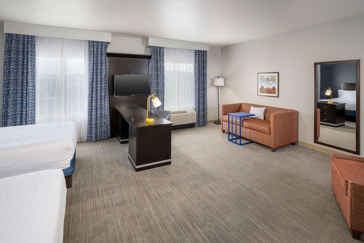 A hotel room with a bed, a desk, a sofa, a TV, and a mirror.