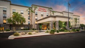 Un hotel Hampton Inn & Suites con una fachada moderna, palmeras y un área de entrada bien cuidada.