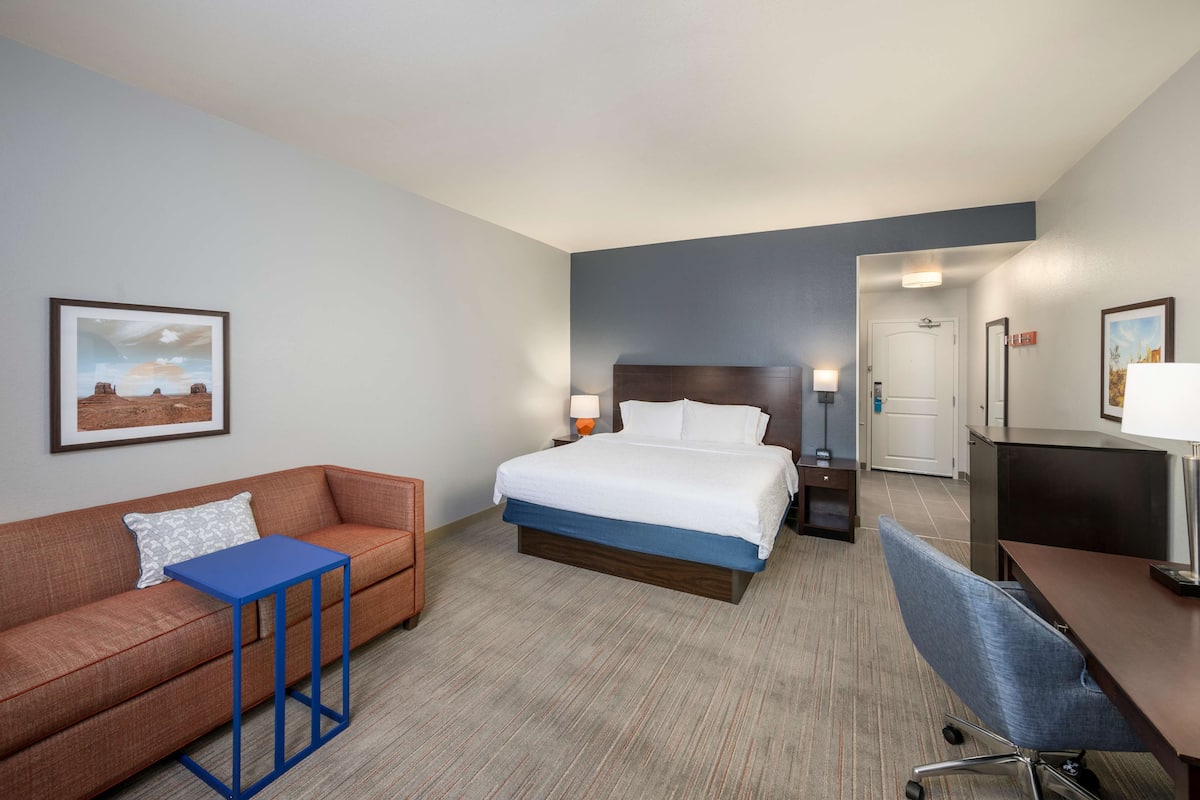 A hotel room with a bed, a sofa, a desk, and a chair.