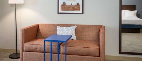 A room with a sofa, a small table, a lamp, and a framed picture on the wall.
