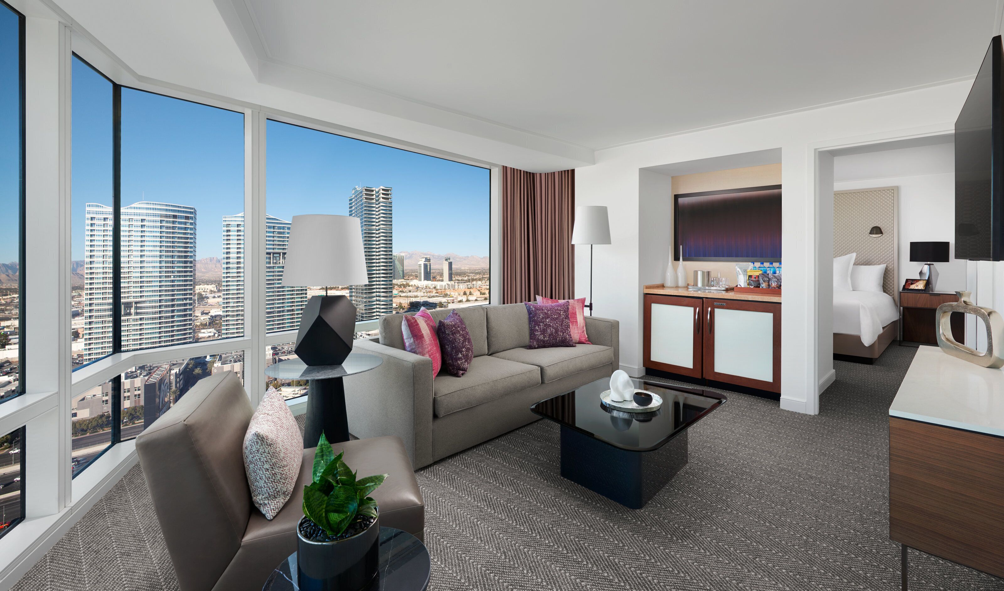 A modern hotel room with a sofa, a coffee table, a TV, and a dining area.