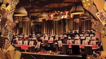 A casino with multiple blackjack tables, striped chairs, and card-themed lighting.