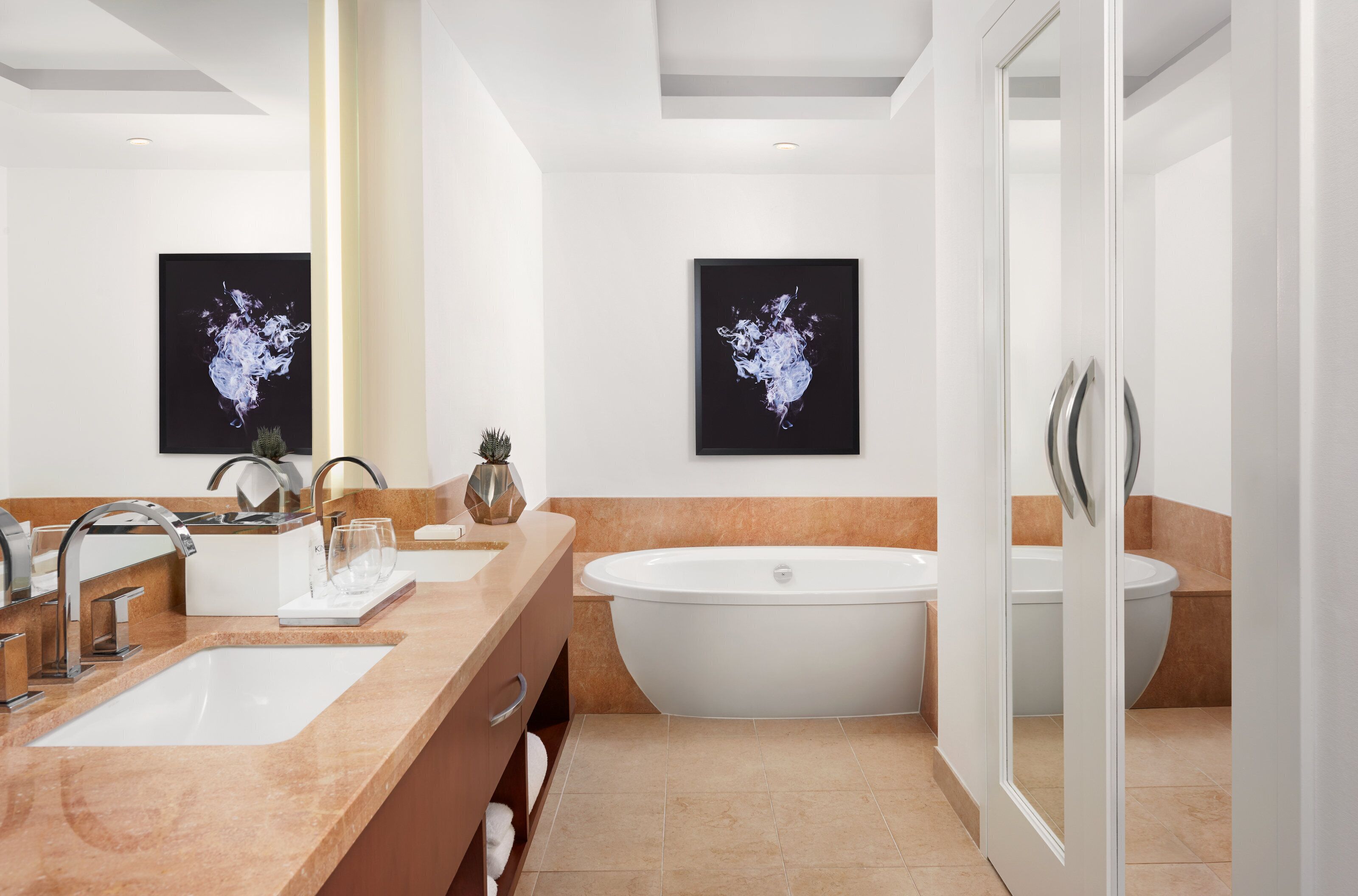 A modern bathroom with a freestanding bathtub, a double sink vanity, and two framed abstract paintings on the wall.
