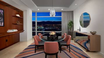 Un comedor moderno con una mesa redonda de vidrio, seis sillas, un ventanal con vistas a la ciudad, un armario de madera y un espejo decorativo.
