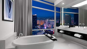 A modern bathroom with a large bathtub, a vanity with a mirror, and a view of a cityscape at night.