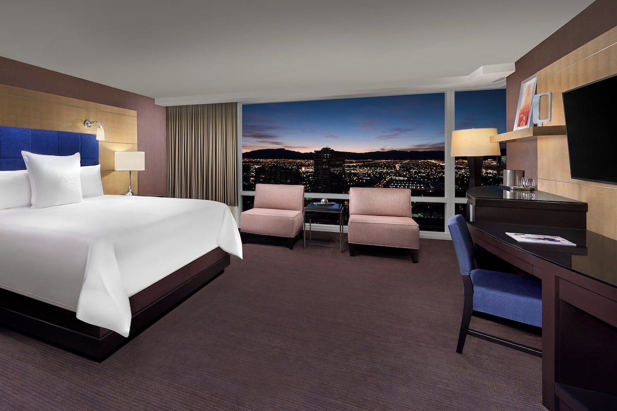 A hotel room with a large bed, two armchairs, a desk, and a city view.