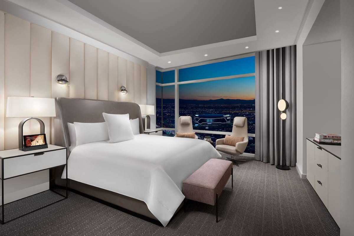 A modern hotel room with a large bed, bedside tables, a desk, and a view of the city at night.
