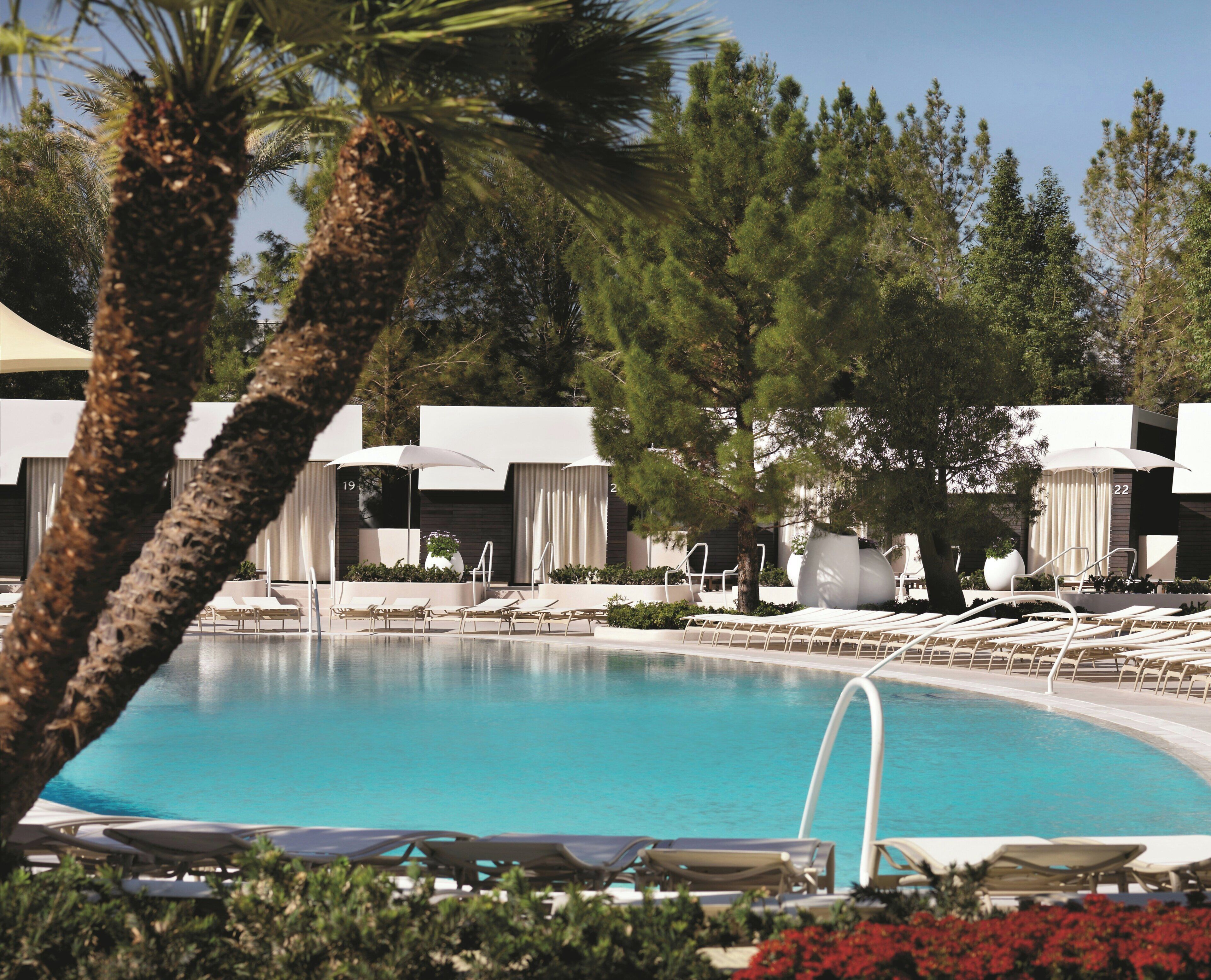 A pool area with lounge chairs and umbrellas, surrounded by trees and a modern building.