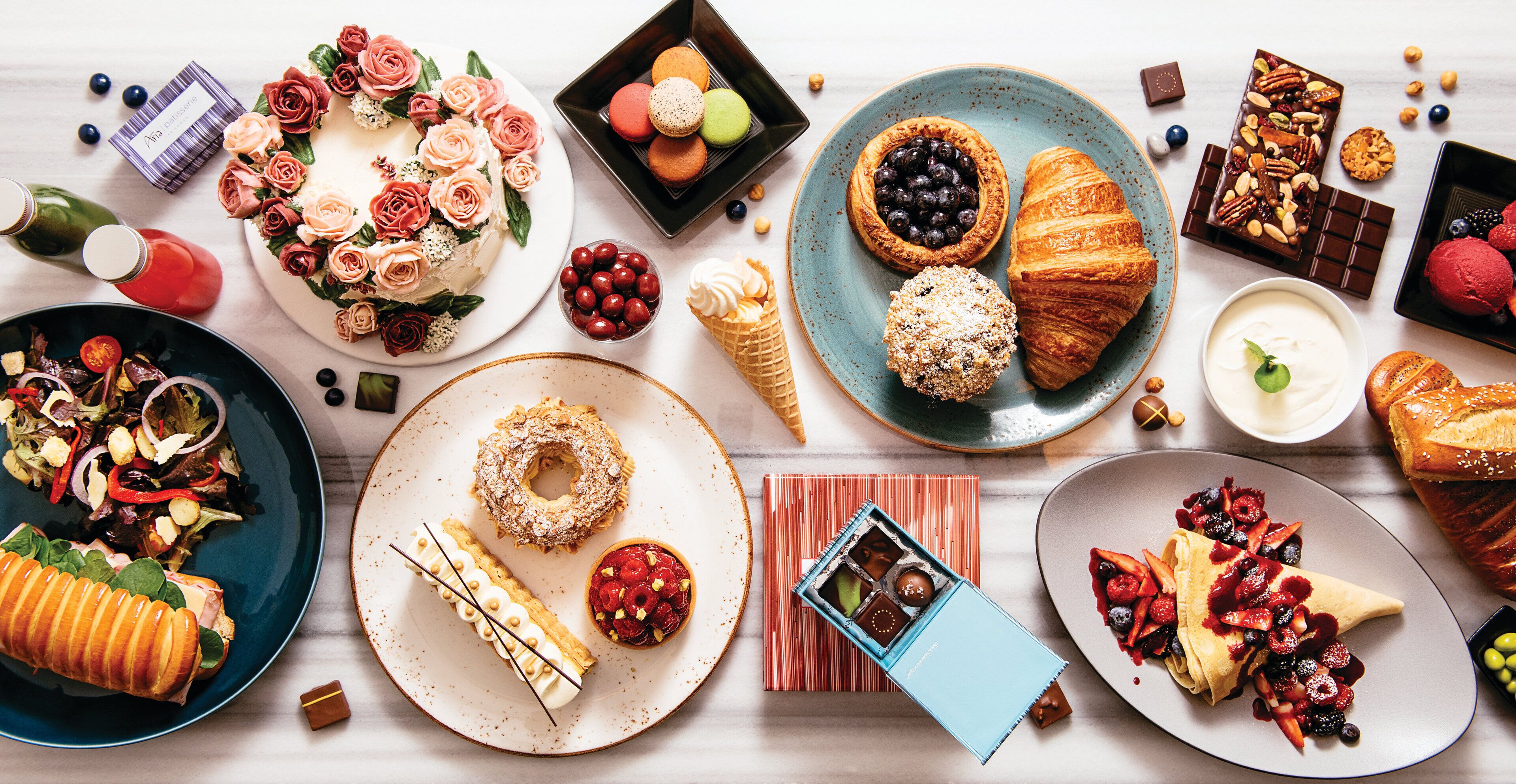 Une variété de desserts et de pâtisseries présentés sur des assiettes, notamment un gâteau décoré de roses, un croissant et une tarte aux fruits rouges.