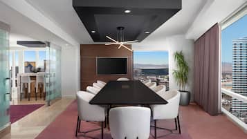 A modern conference room with a large table, white chairs, a mounted TV, and a city view.