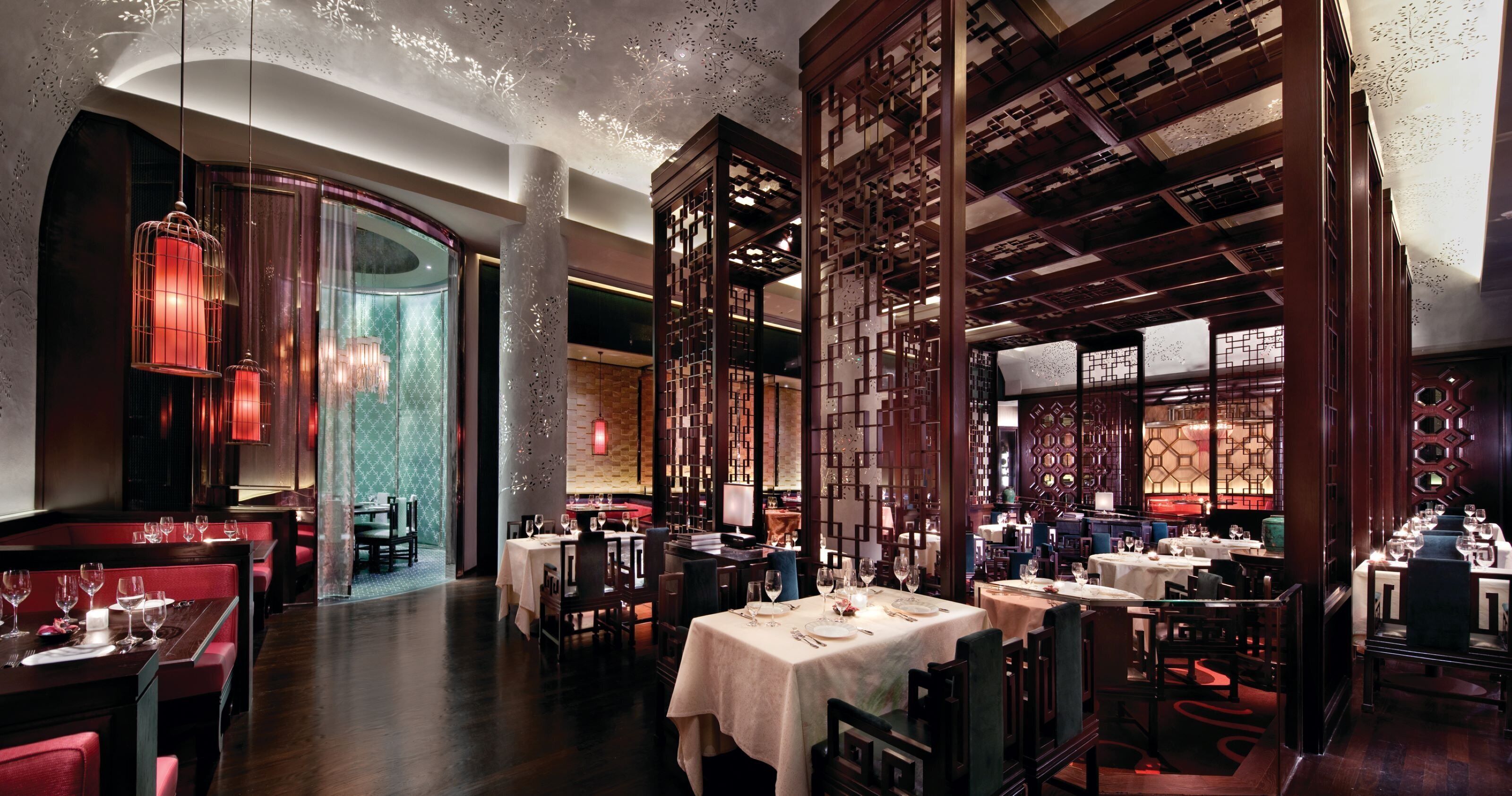 L’intérieur d’un restaurant présente de nombreuses tables, des banquettes rouges recouvertes de tissu et des cloisons en bois de style traditionnel.