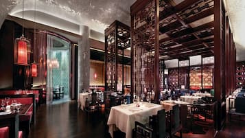 Interior de restaurante con varias mesas, asientos tapizados en rojo y separadores de madera tradicional.