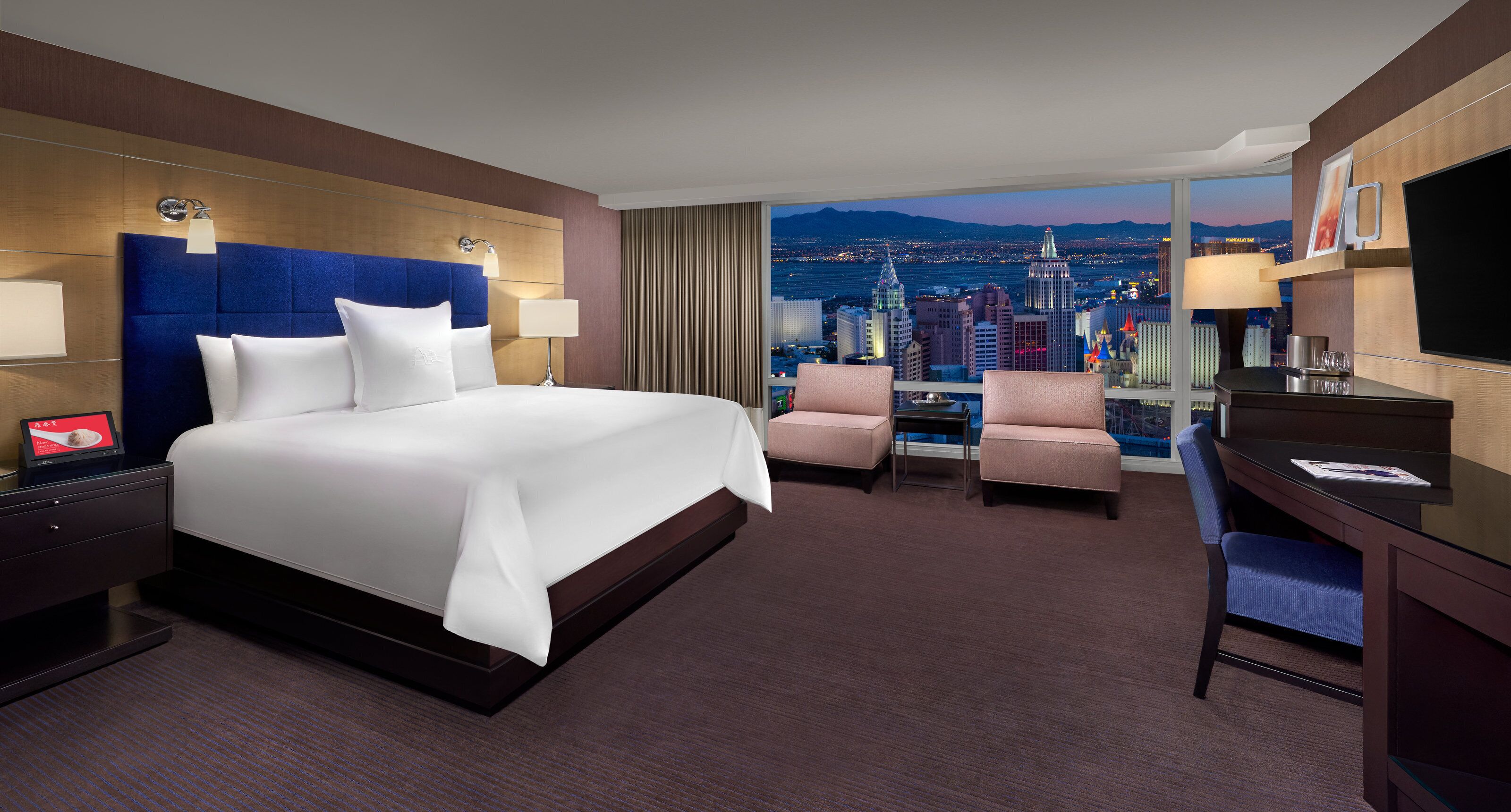 Een hotelkamer met een groot bed, twee fauteuils, een bureau en uitzicht op de stad.