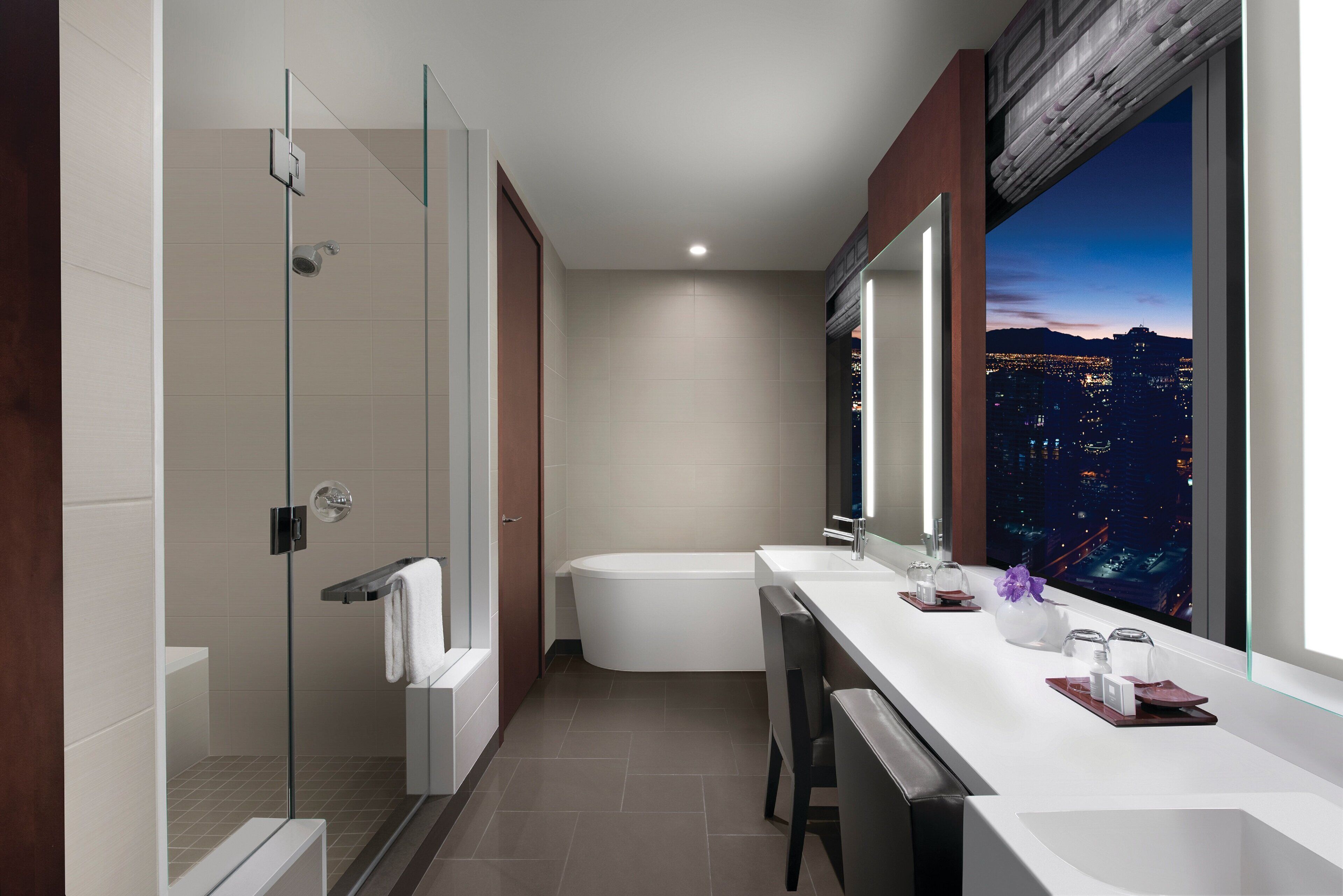 Un baño moderno con ducha de vidrio, bañera y tocador con un amplio ventanal que ofrece vistas a la ciudad.